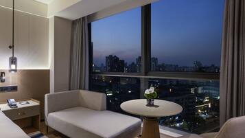 A modern hotel room with a large window offering a city view at dusk.