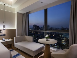 A modern hotel room with a large window offering a city view at dusk. - Novotel Shanghai Jingan (Shanghai)