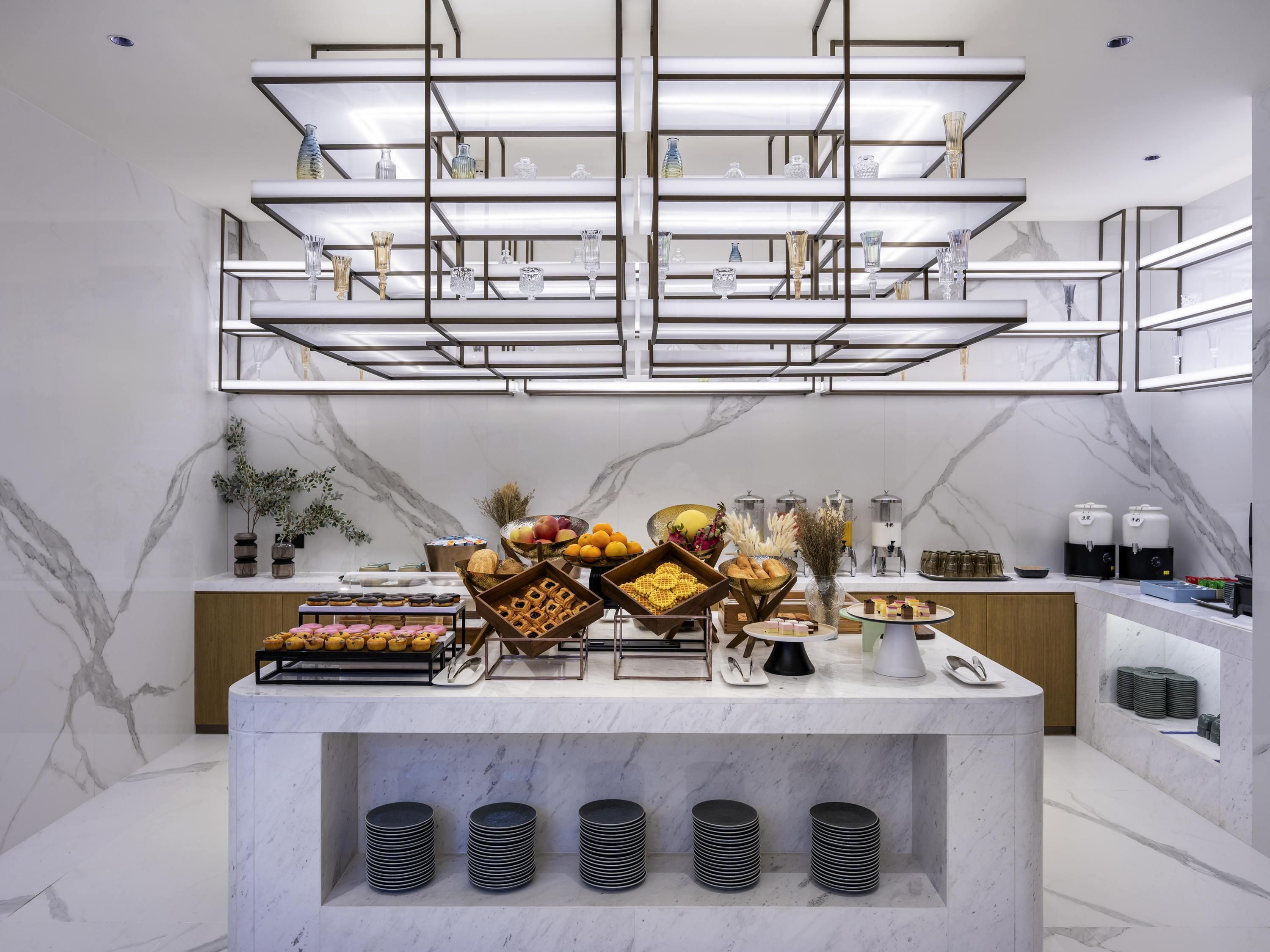 Una cocina moderna con encimeras de mármol, una isla central con alimentos y bebidas, y una vitrina de vidrio arriba.