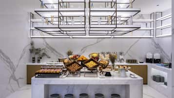 Una cocina moderna con encimeras de mármol, una isla central con alimentos y bebidas, y una vitrina de vidrio arriba.