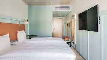 A modern hotel room with a large bed, a TV mounted on the wall, and a small table with a lamp.