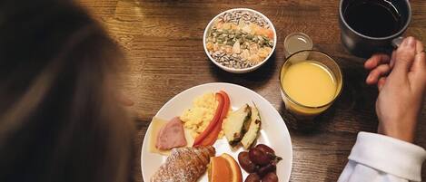 A dining table with a plate of breakfast food, a potted plant, and a glass of juice.