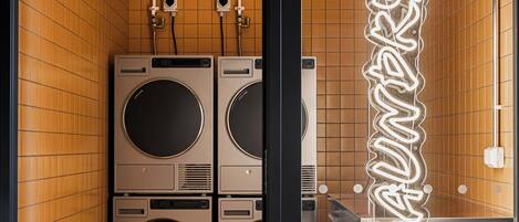 A compact laundry room with two stacked washing machines and a neon sign reading "laundry".