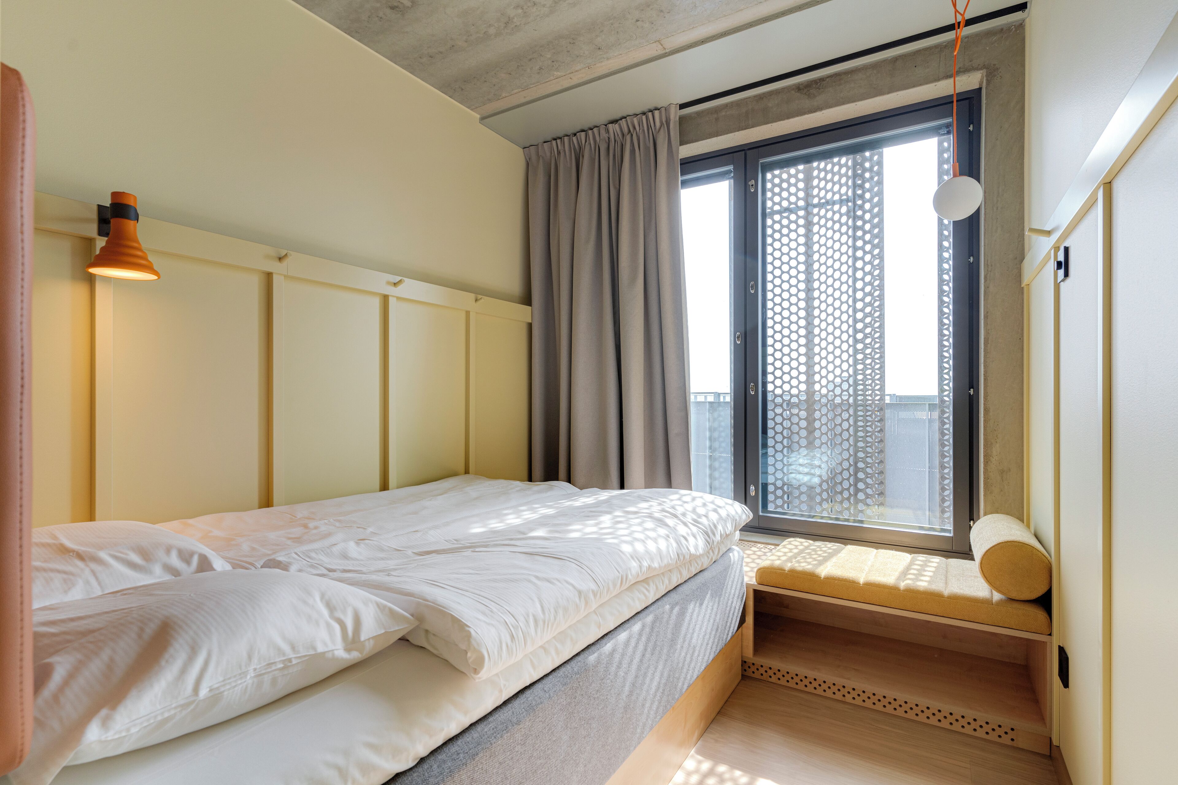 A bedroom with a bed, a window with a view, a bedside table, and a hanging light fixture.