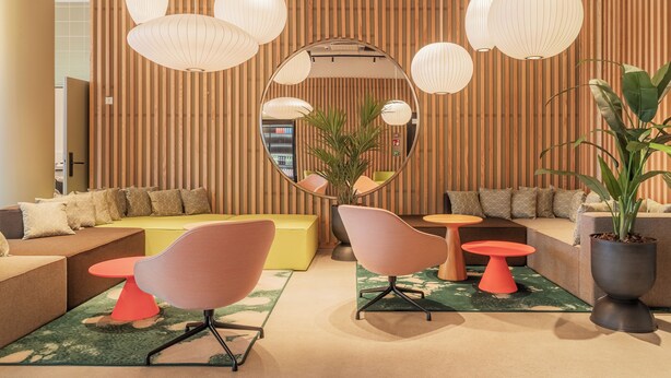 Un área de descanso moderna con un espejo circular, paredes de listones de madera y diversas opciones de asientos, incluyendo sofás y sillones.