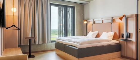 Una habitación de hotel moderna con una cama grande, una mesita de noche, un televisor y una ventana con cortinas.