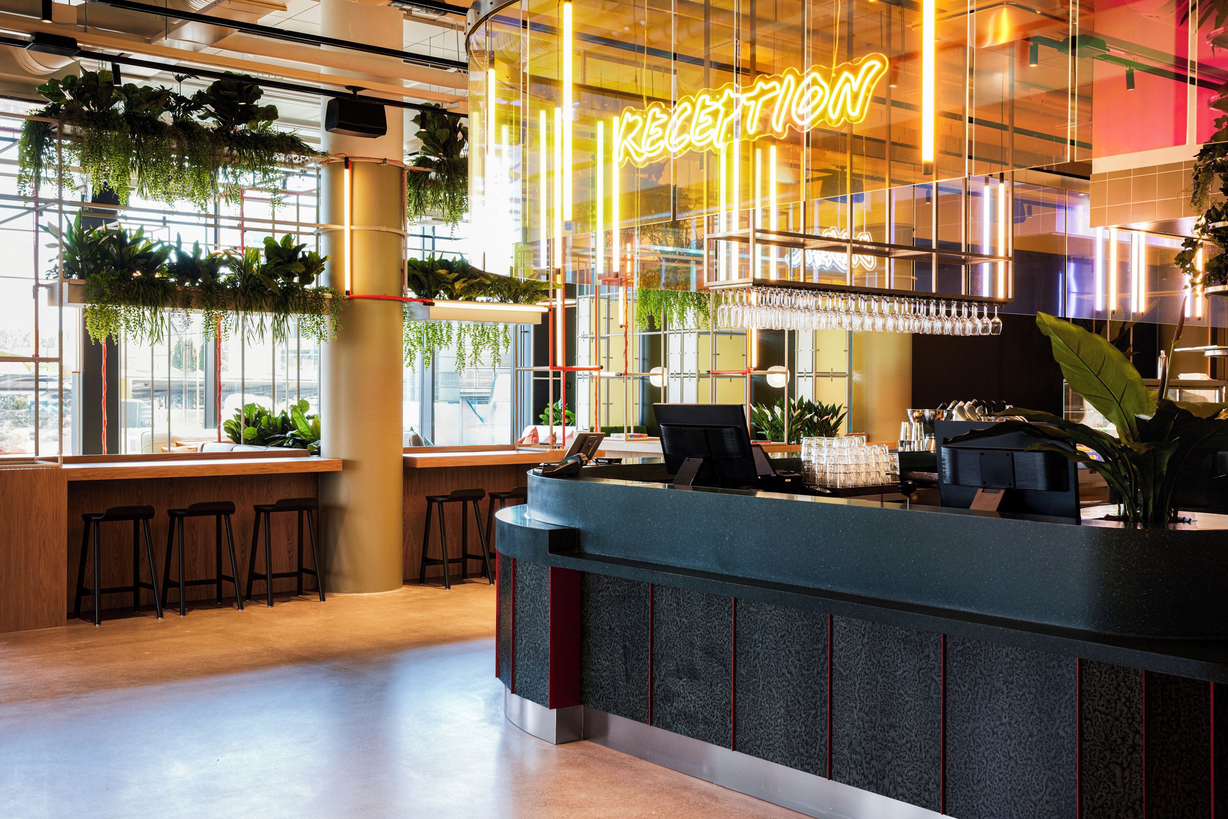 A modern reception area with a neon sign, bar stools, and a counter with a computer and glassware.