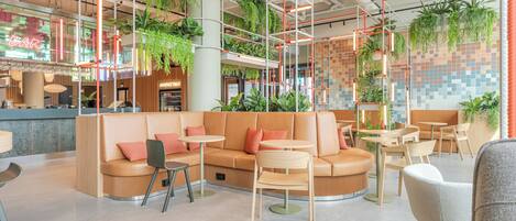 Un espacio interior moderno con zonas de estar, mesas y plantas colgantes.