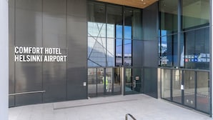 Exterior del Comfort Hotel en el Aeropuerto de Helsinki, con grandes puertas de vidrio, una fachada moderna y el terminal del aeropuerto a la vista.