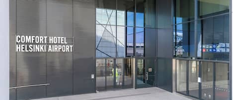 Exterior del Comfort Hotel en el Aeropuerto de Helsinki, con grandes puertas de vidrio, una fachada moderna y el terminal del aeropuerto a la vista.