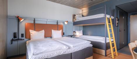 A modern hotel room with two beds, a bunk bed, a wooden ladder, and a small desk with a lamp.