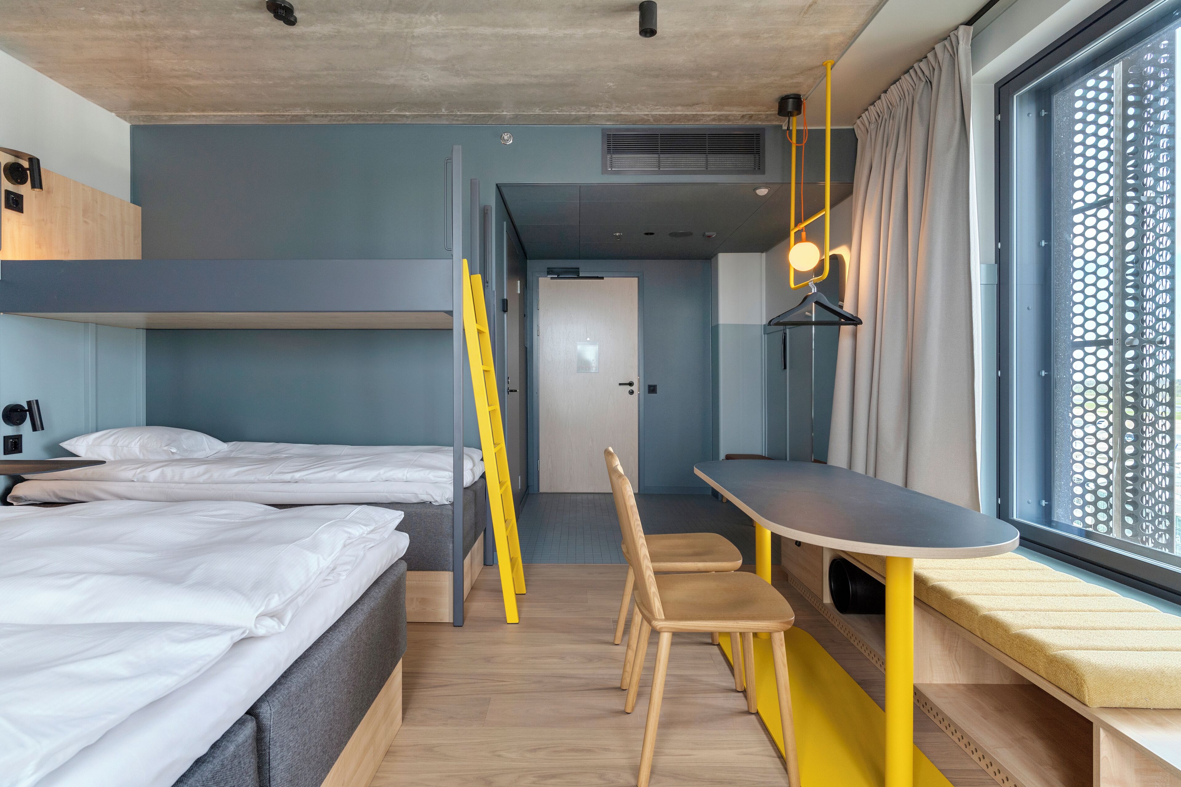 A compact hotel room with bunk beds, a desk, and a window with a view.