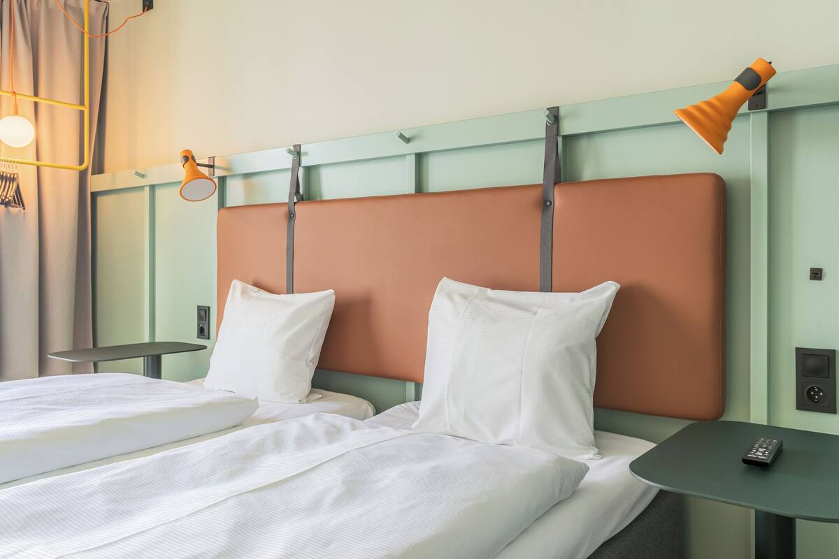 Habitación de hotel con dos camas, una mesita, una lámpara y un panel de control en la pared.