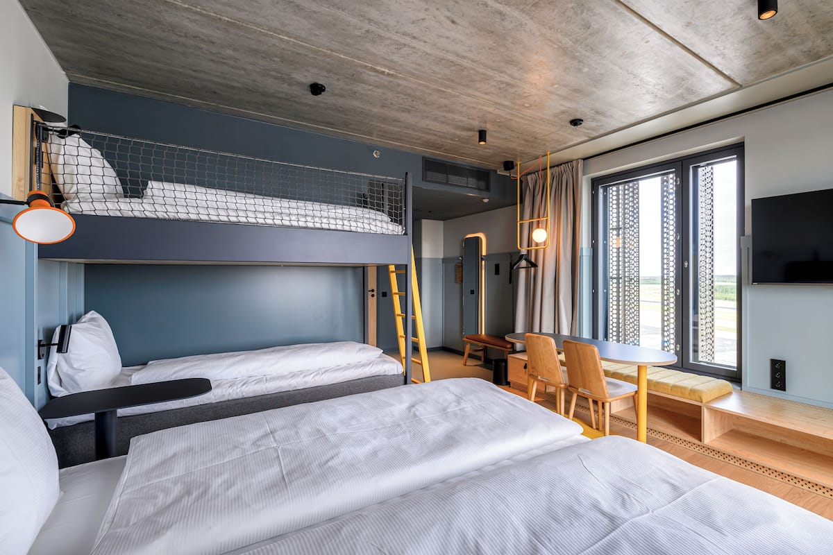 Una habitación de hotel moderna con literas, un escritorio y un ventanal grande con cortinas.