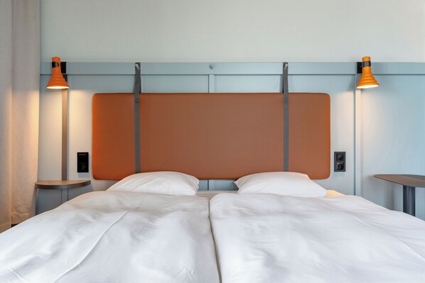 Una cama doble con cabecera, dos mesitas de noche y dos lámparas de pared.