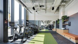 Un gimnasio con equipo de ejercicio, un sendero de césped artificial verde y una zona de recepción con un banco y plantas en macetas.
