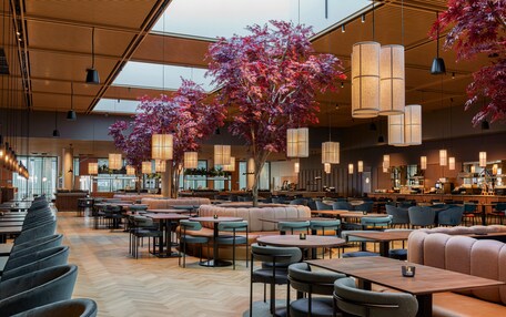 A spacious restaurant with high ceilings, modern pendant lighting, and a central seating area with a large tree.