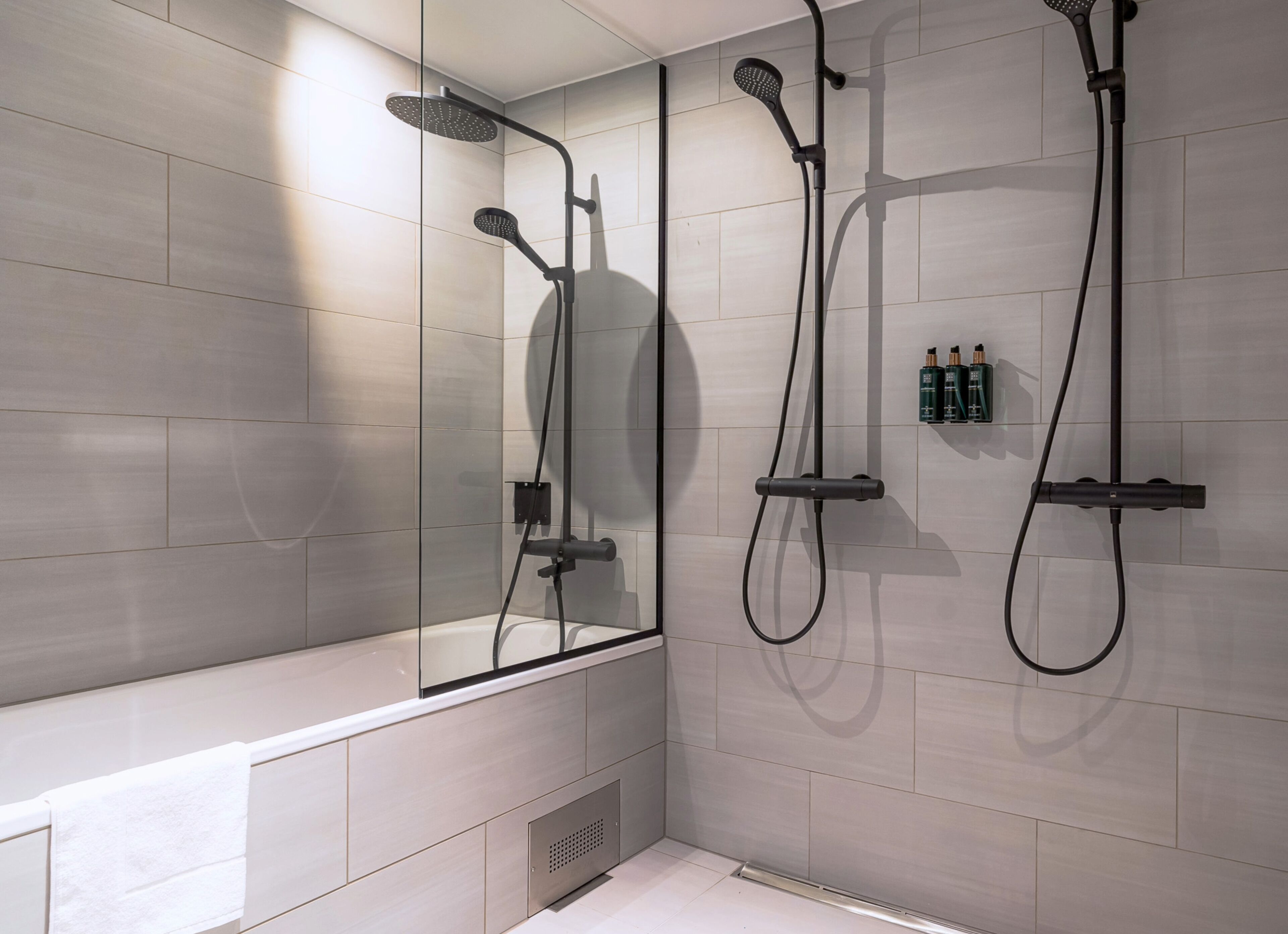 Une salle de bain moderne avec une douche à parois de verre, une baignoire et une étagère murale où sont rangés les articles de toilette.