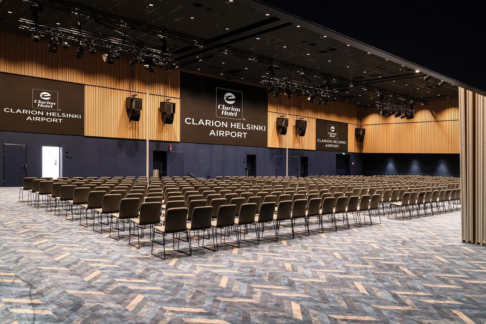 A large conference room with rows of chairs, a stage with lighting, and the Clarion Helsinki Airport sign on the walls.