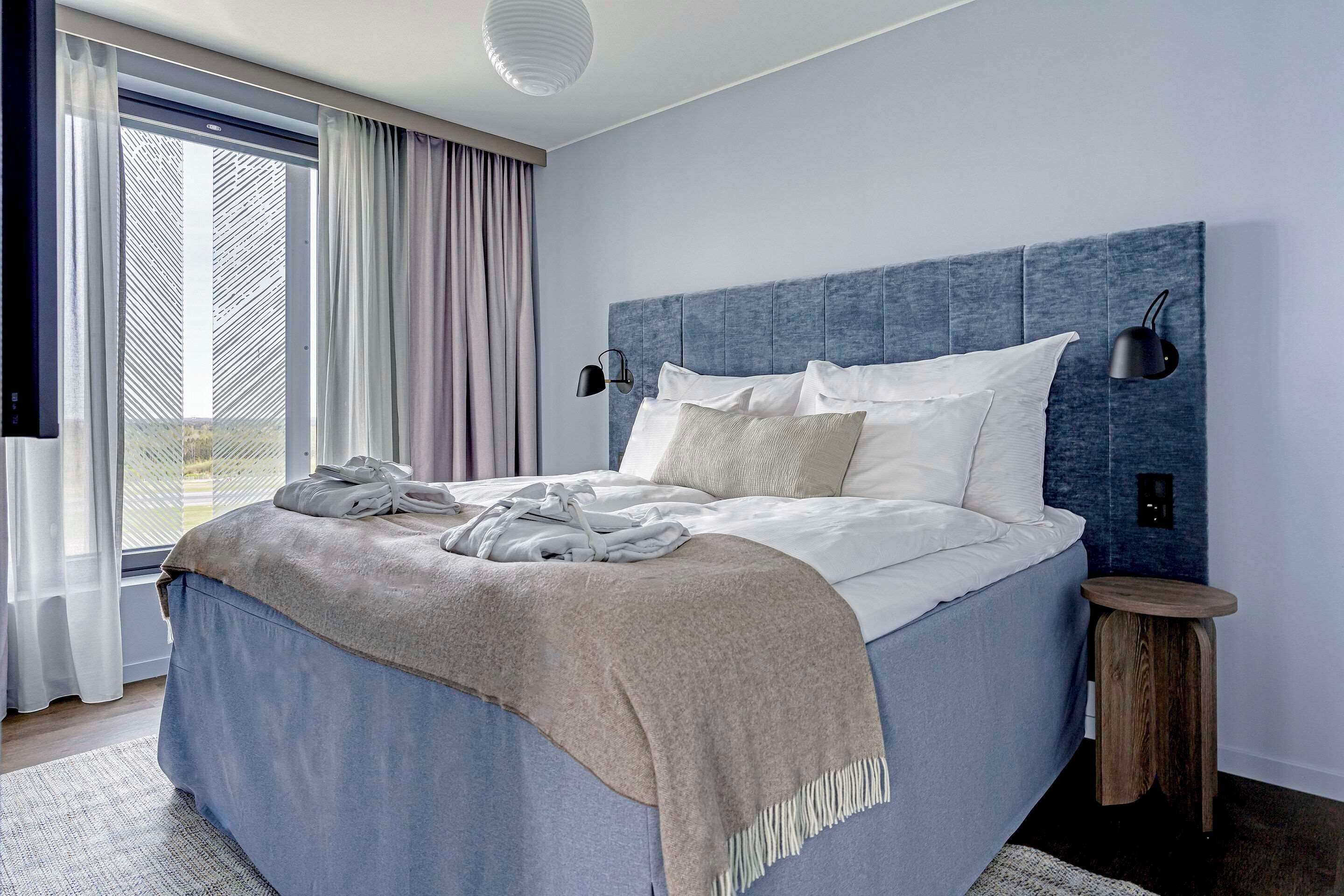 Un dormitorio moderno con una cama grande, cabecera, mesita de noche y vistas al exterior a través de una ventana.