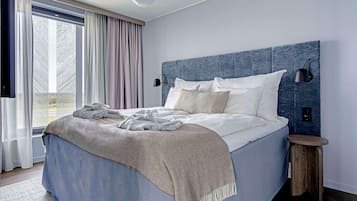 Ein modernes Schlafzimmer mit einem großen Bett, einem Kopfteil, einem Nachttisch und Blick ins Freie durch ein Fenster.
