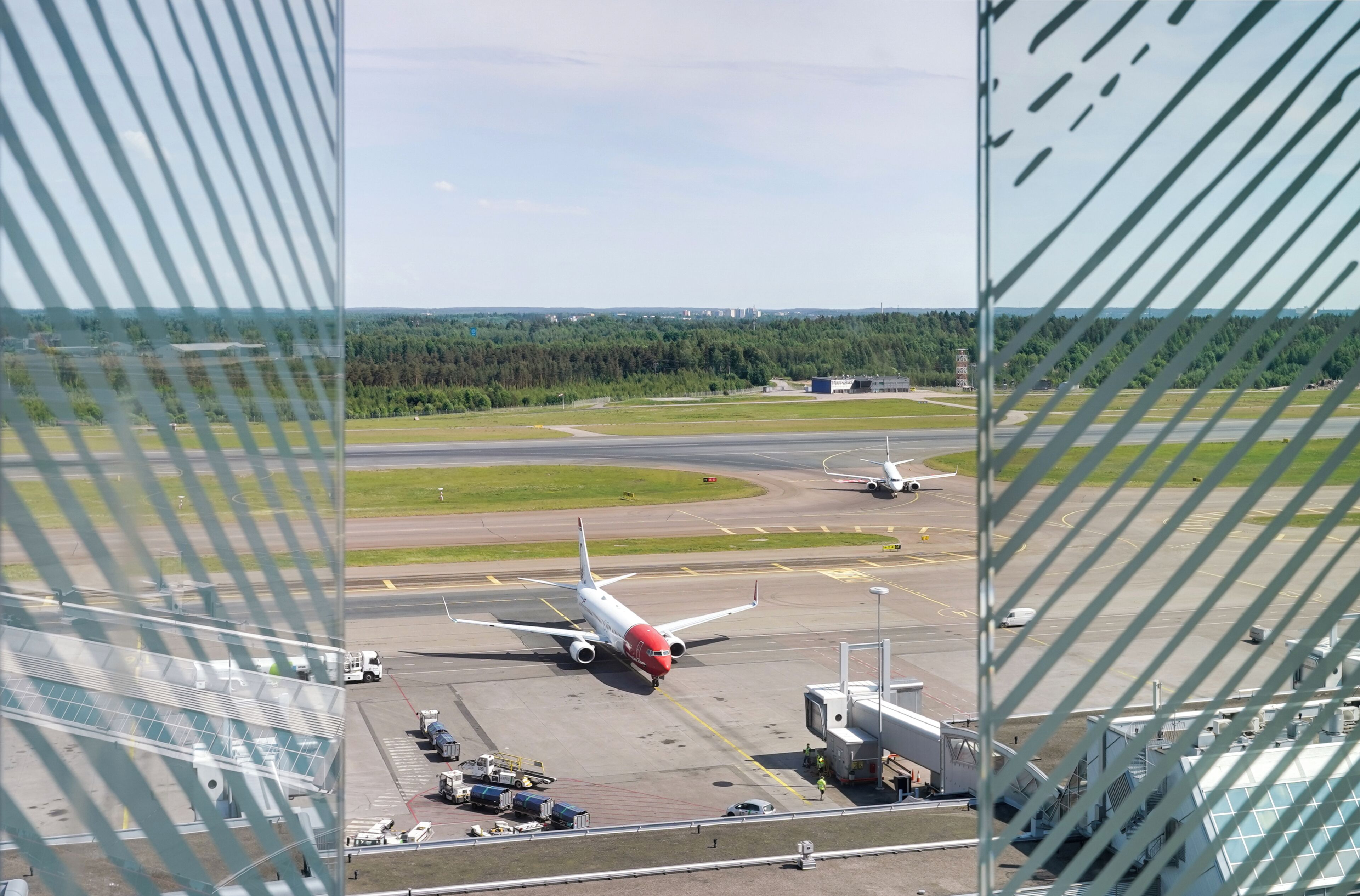 An airport runway with an airplane taxiing, airport buildings, and a clear sky.