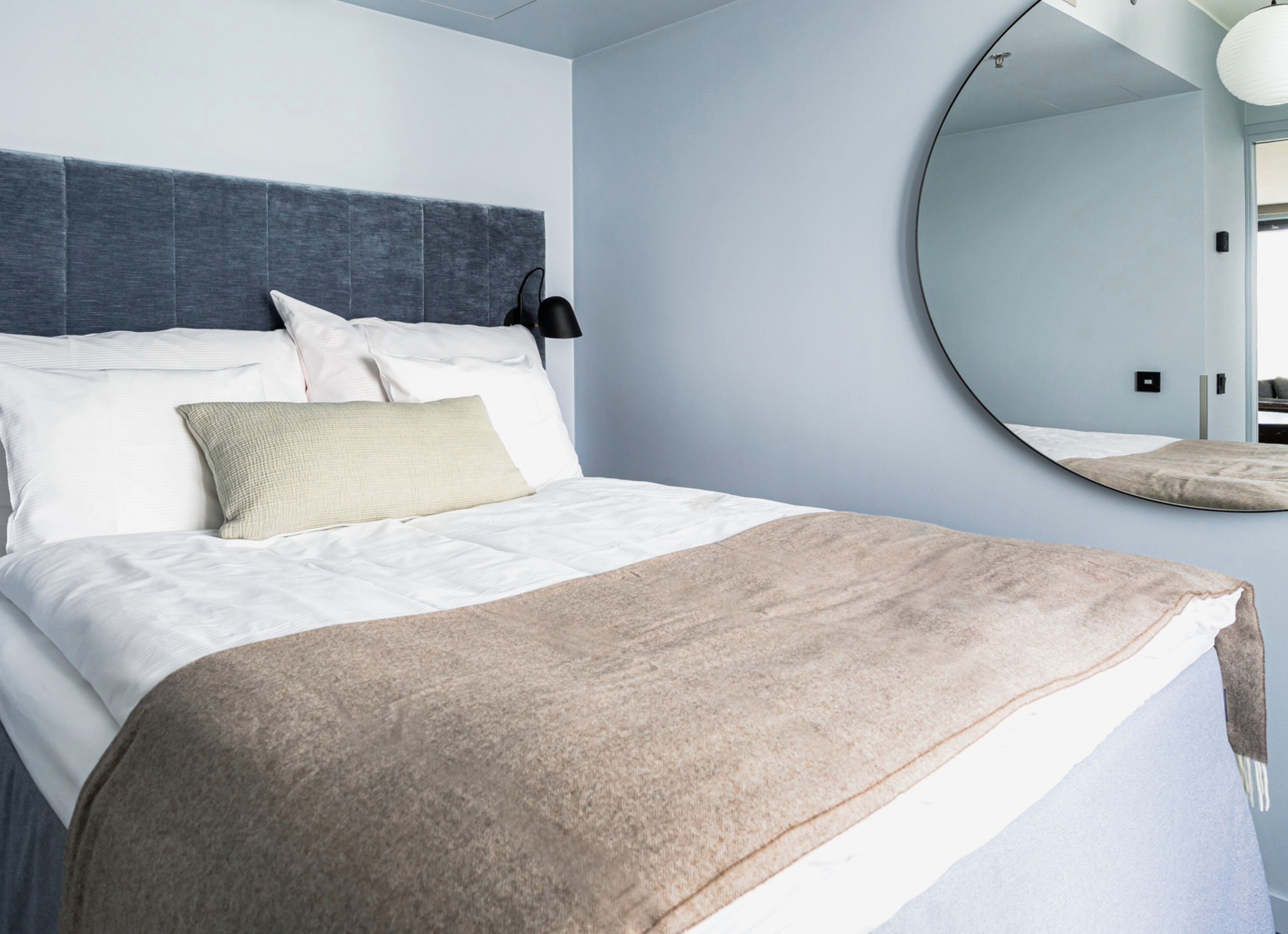 A modern bedroom with a large bed, a round mirror, and a headboard.