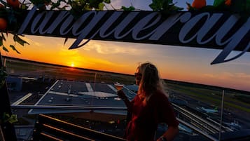 Henkilö seisoo parvekkeella, jolta avautuu näkymä lentokentälle ja auringonlaskuun.