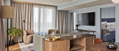 Una habitación de hotel moderna con sofá, una mesa de centro de madera, una mesa de comedor y un televisor.