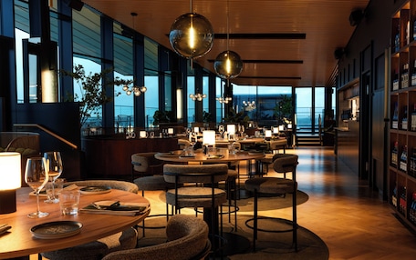 A modern restaurant with round tables, chairs, and pendant lighting.