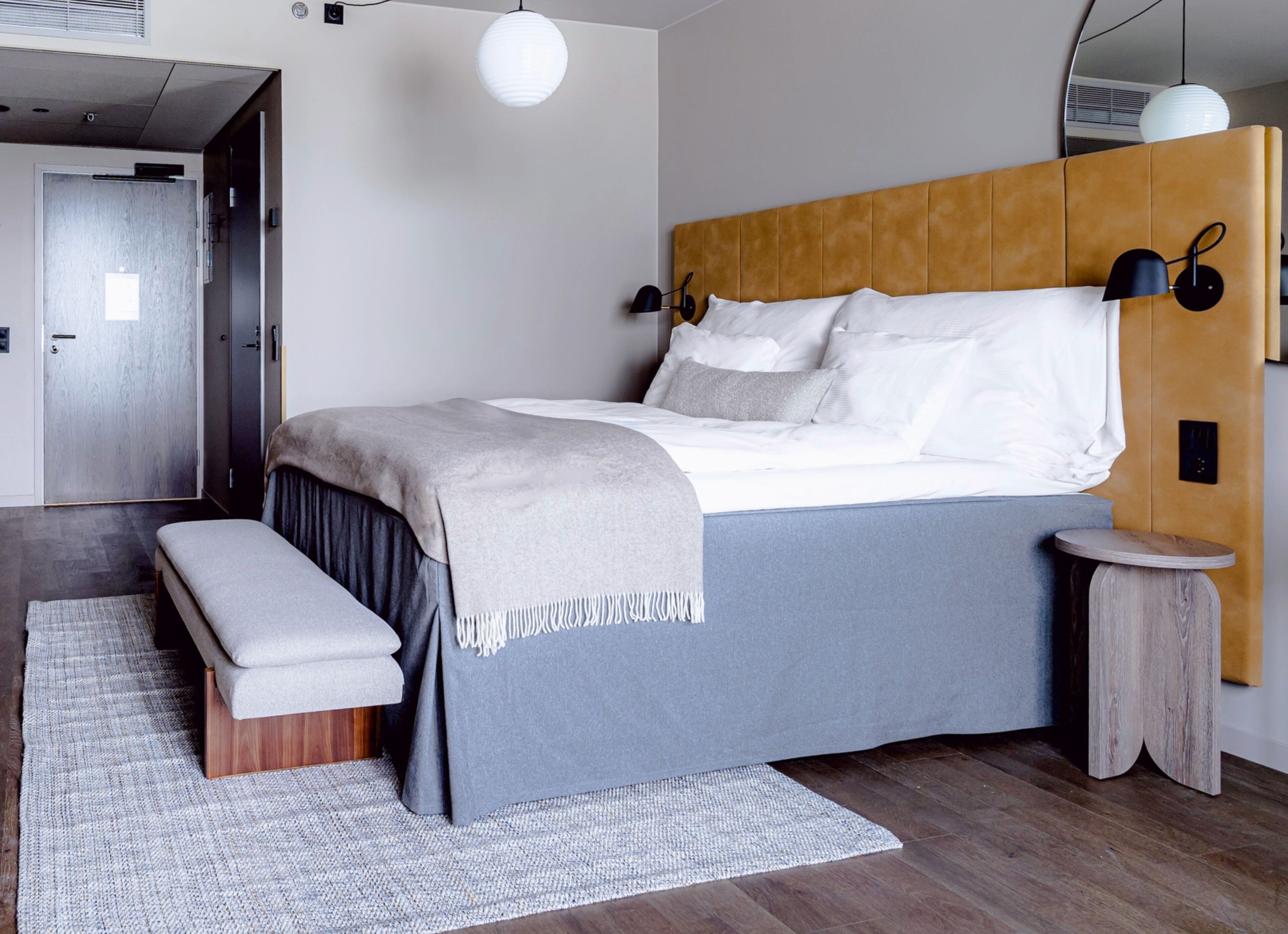 A modern bedroom with a large bed, a bench, a bedside table, and a small stool.