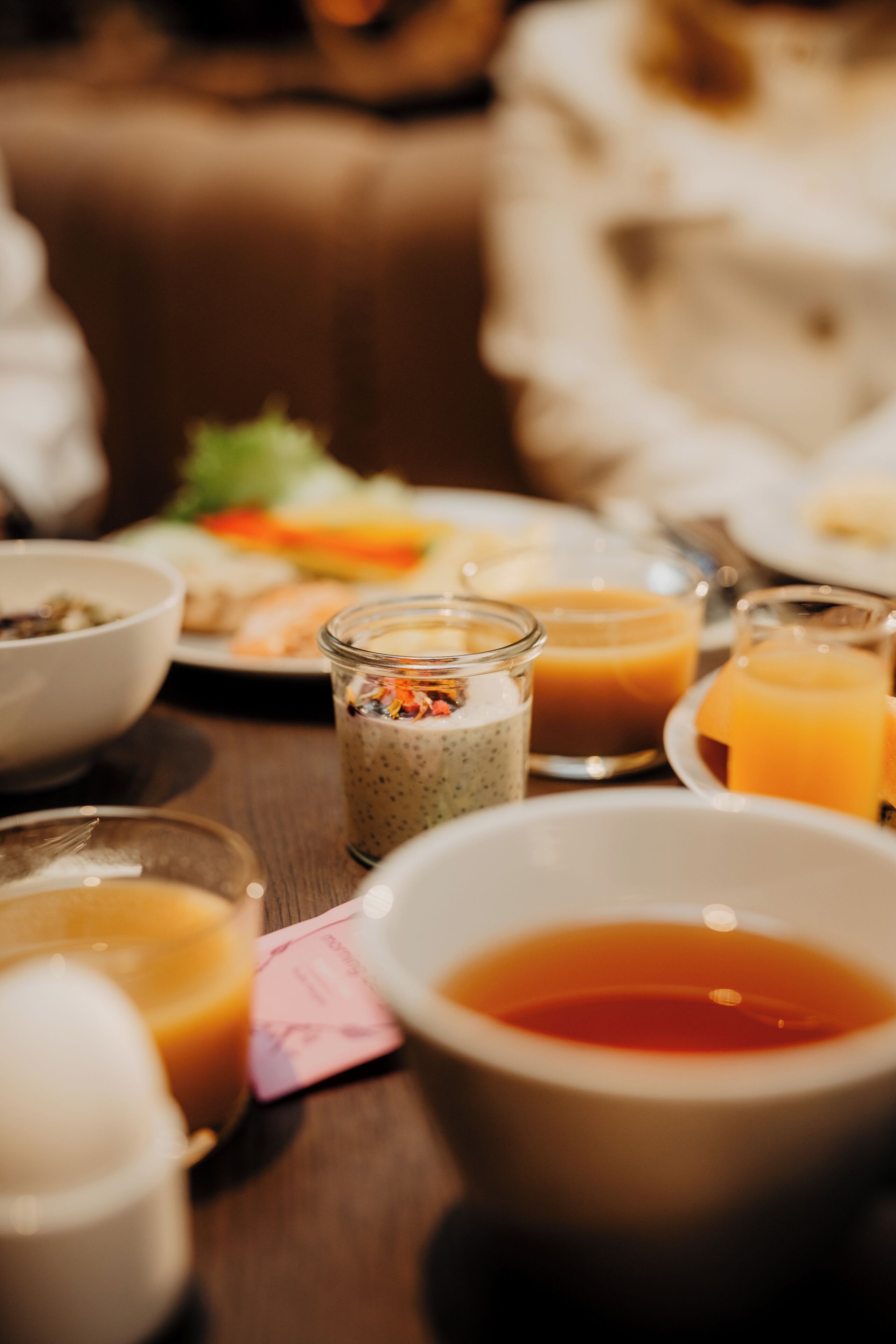 A dining table with various food items and beverages, including bowls, glasses, and a small jar.