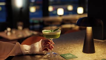A cocktail in a glass with a green liquid and a garnish, held by a hand.