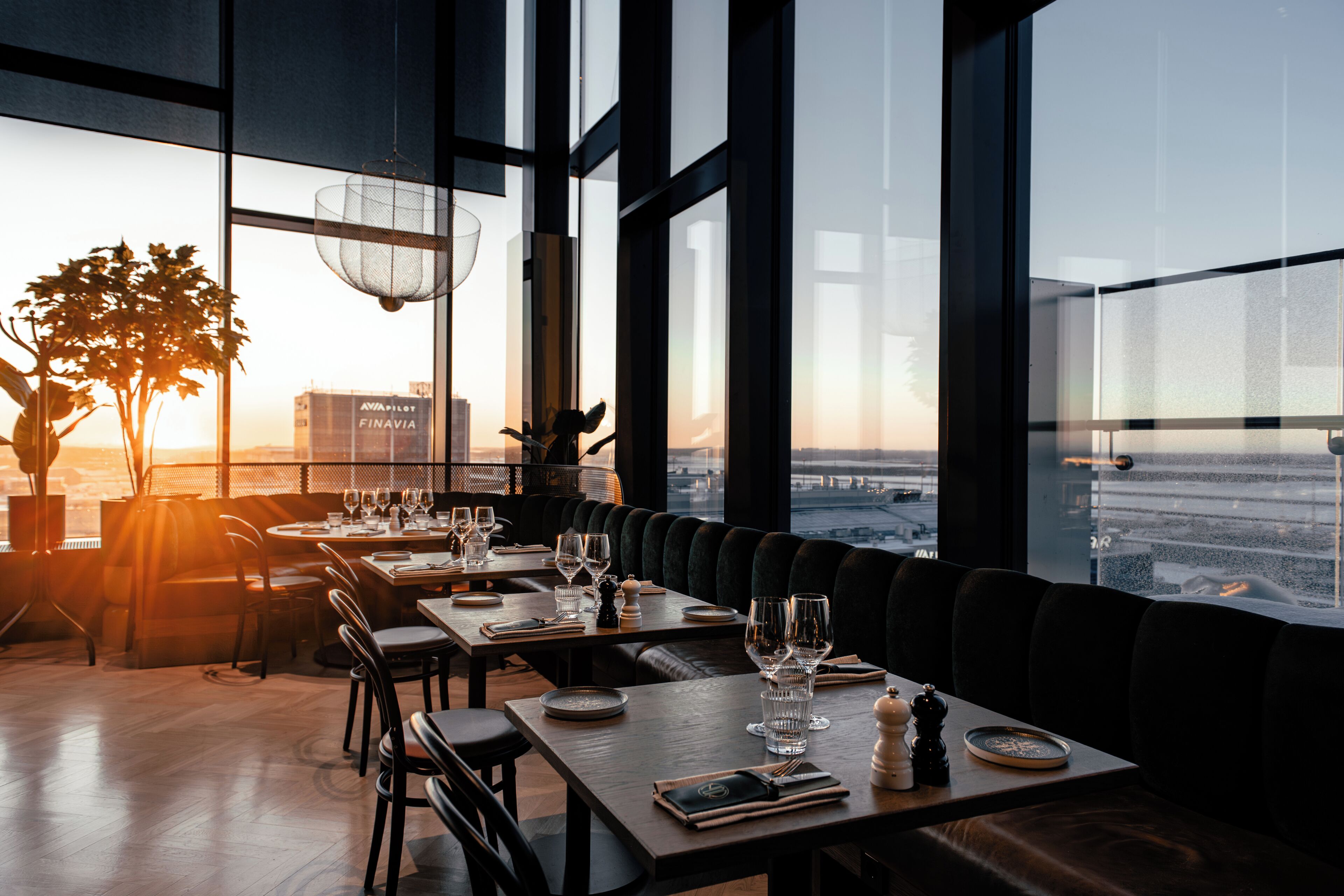 Un restaurante con mesas dispuestas para comer, amplios ventanales y vistas a la ciudad.