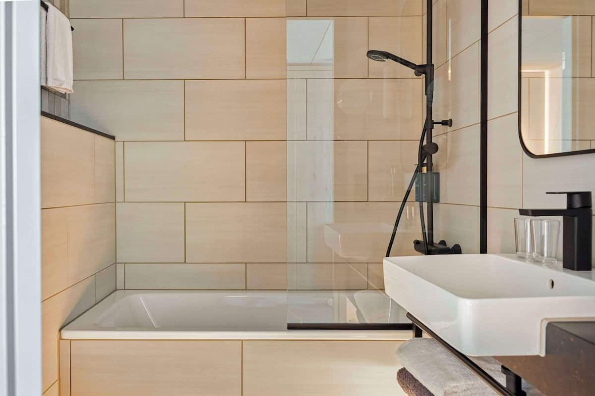 Ein modernes Badezimmer mit einer gläsernen Duschkabine, einem weißen Waschbecken und einem Spiegel darüber.
