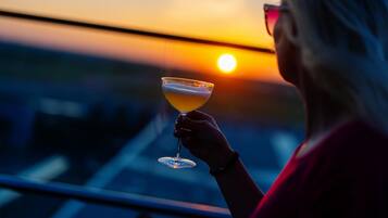 Henkilö, jolla on kädessään cocktail-lasi ja taustalla näkyy auringonlasku.