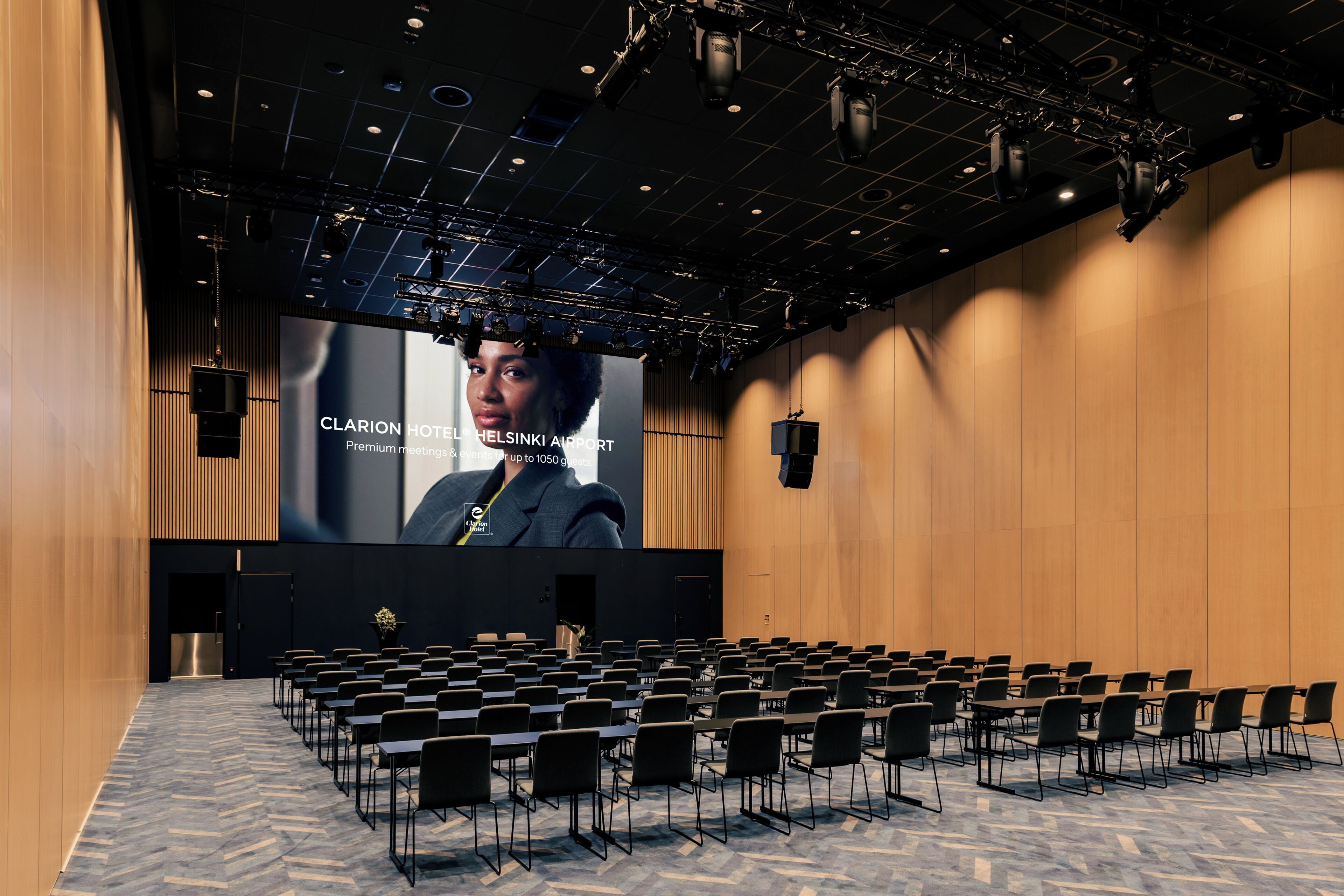 A conference room with rows of chairs, a large screen, and a stage with lighting equipment.