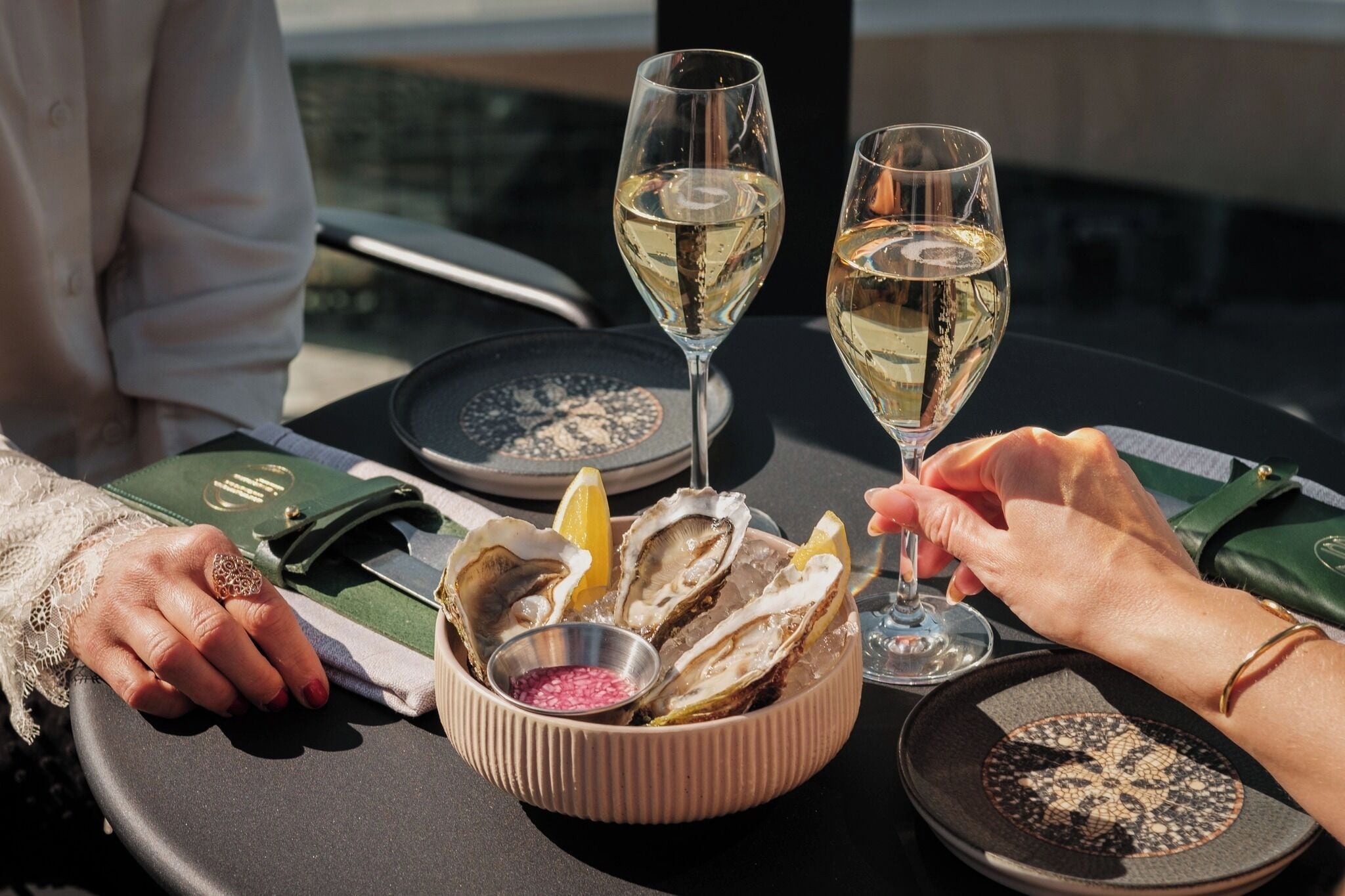 A dining table with oysters, glasses of white wine, and a menu.