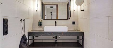 Un baño moderno con un espejo grande, un lavabo y un cabezal de ducha manual.
