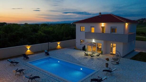 Una casa moderna de dos pisos con piscina, mobiliario exterior y vistas al paisaje circundante.