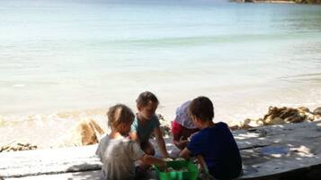 Trois enfants jouent près d’une plage, sur un rivage rocheux, au bord d’une mer calme.