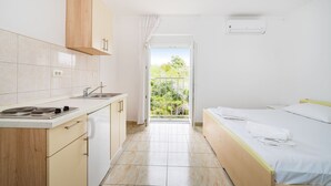 A compact room with a kitchenette, a bed, and a balcony with a view of greenery.