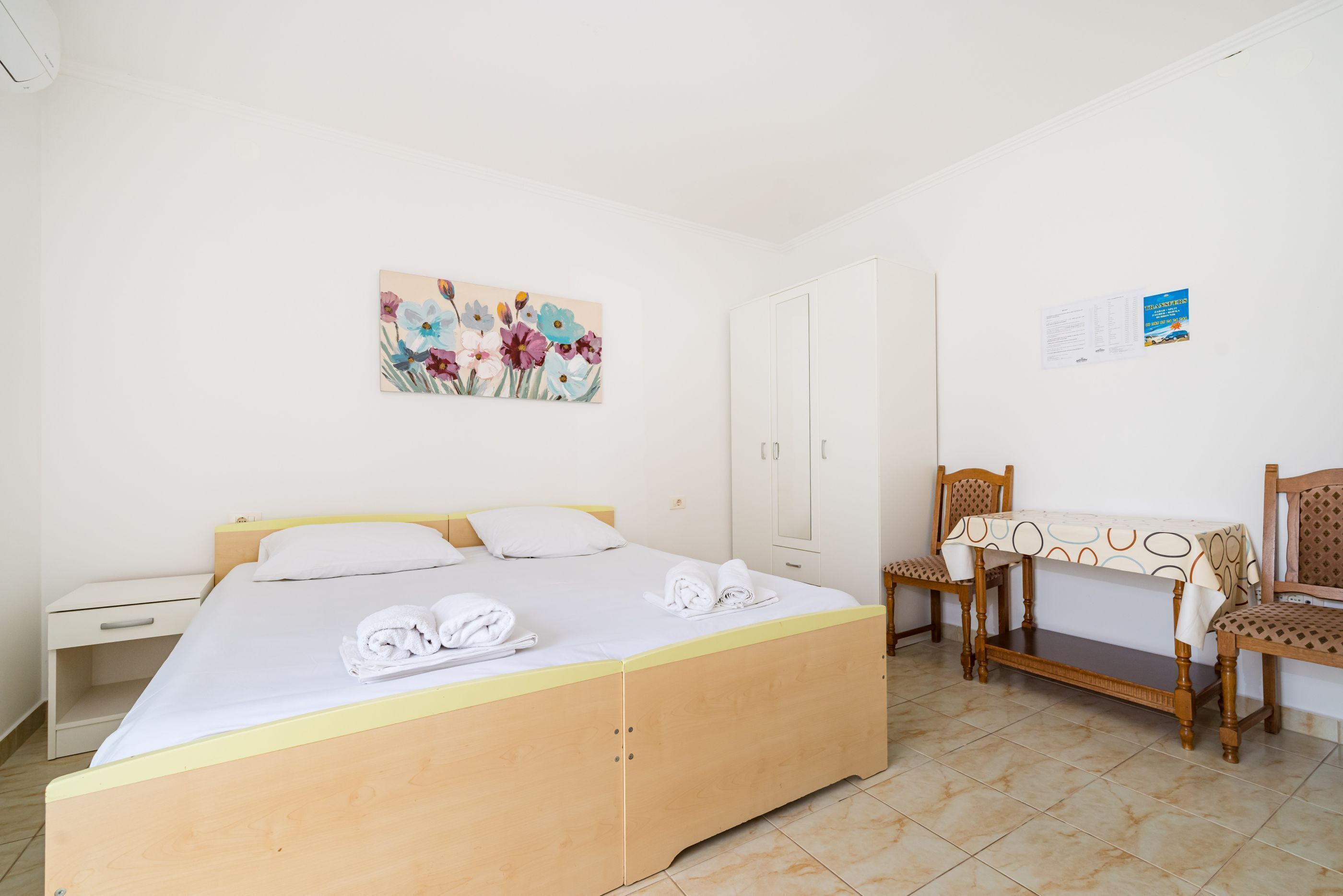 A bedroom with a bed, a desk, a chair, and a wall-mounted painting.