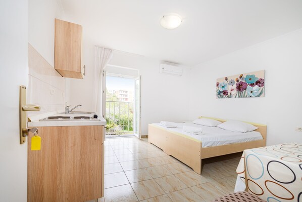Ein Schlafzimmer mit Bett, Fenster, einem Bild und einer Küchenzeile.
