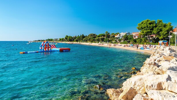 Una playa costera con aguas cristalinas, un litoral rocoso y una pequeña estructura inflable.