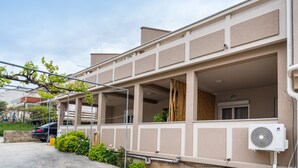 Un edificio residencial con balcón, un automóvil estacionado y un equipo de aire acondicionado.