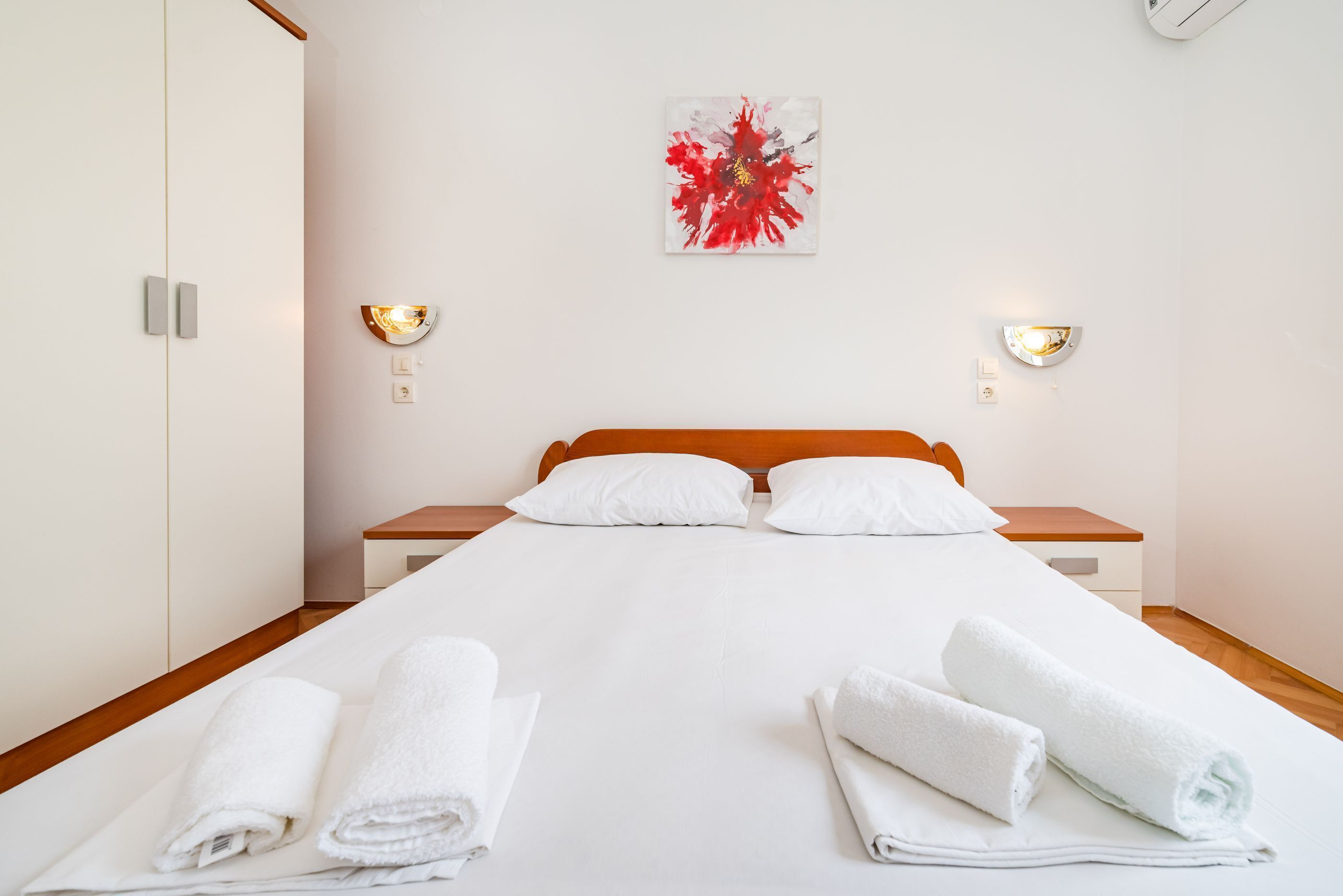 A hotel room with a bed, two bedside tables, a wall-mounted artwork, and two wall sconces.