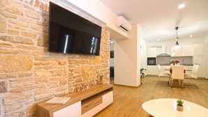 Una sala de estar moderna con una pared de piedra, un televisor de pantalla plana, un mueble bajo de madera y un comedor con mesa y sillas.