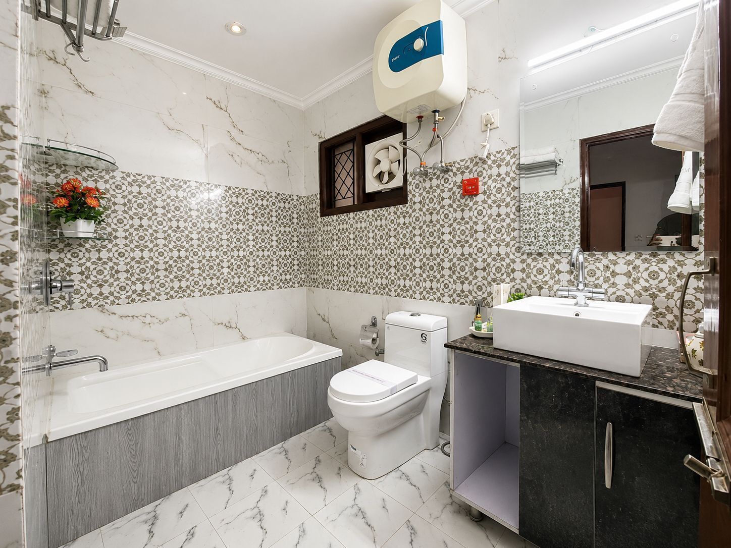 A bathroom with a bathtub, toilet, and sink, marble flooring, and patterned wall tiles.