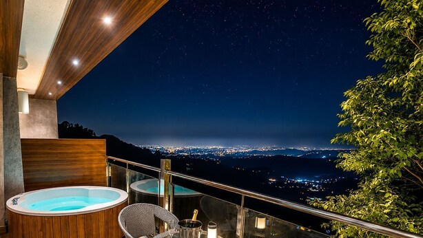 A balcony with a hot tub, wicker chairs, and a table with a bottle of champagne.